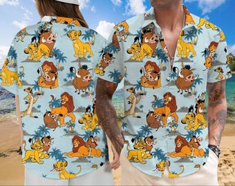 Puede incluir: Una camisa de manga corta con botones azul y blanca con un patrón repetido de leones, hienas y jabalíes de dibujos animados. La camisa tiene cuello y un bolsillo en el lado izquierdo.