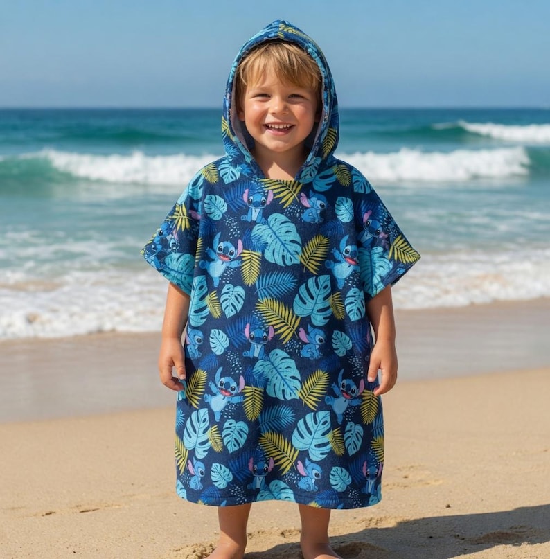 Puede incluir: Un poncho de toalla con capucha en color azul oscuro que presenta un patr&oacute;n repetitivo del personaje Stitch de Lilo y Stitch, intercalado con hojas tropicales de monstera y palmera en azul claro y amarillo, con mangas cortas.