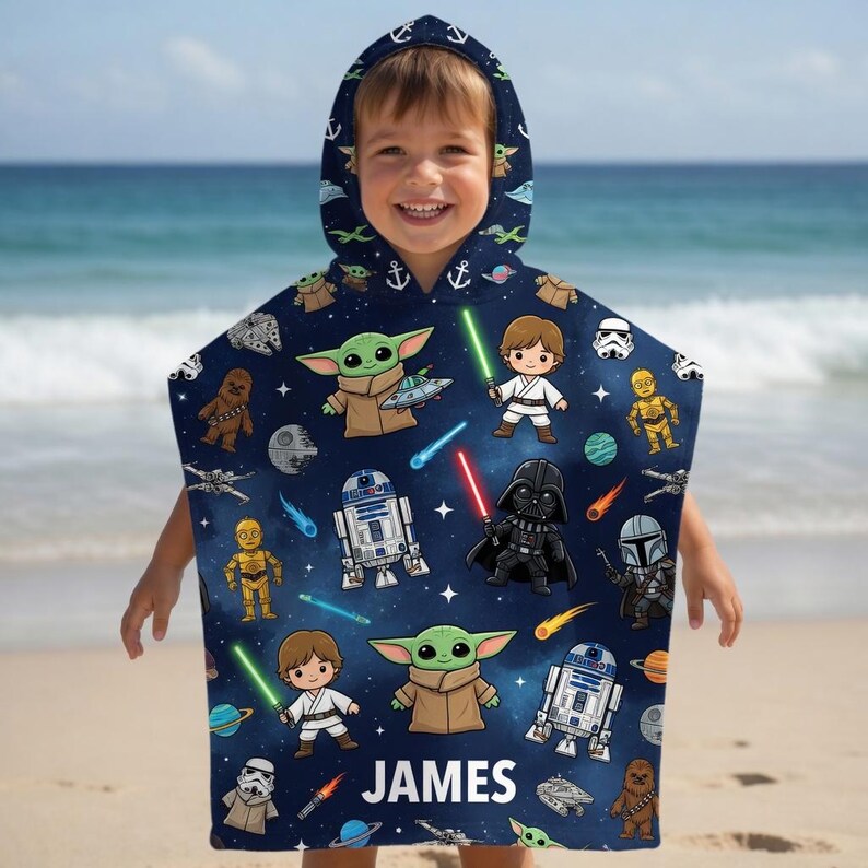 May include: A dark blue hooded poncho towel featuring a repeating pattern of Star Wars characters including Grogu, Luke Skywalker, Darth Vader, R2-D2, C-3PO, and Chewbacca, along with spaceships and lightsabers. The name JAMES is printed in white at the bottom.