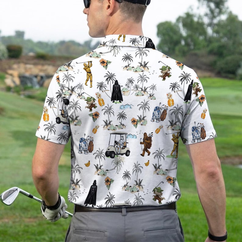 Pu&ograve; includere: Polo da golf bianco con stampa tropicale con personaggi di Star Wars, palme e golf cart. La camicia ha un colletto button-down e maniche corte. La persona nell'immagine indossa la camicia su un campo da golf.