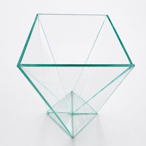 Op de afbeelding: Een helder glazen geometrisch terrarium met een zeshoekige bovenkant en een ruitvormige basis. De randen zijn lichtgroen getint. Het terrarium is ontworpen met scherpe hoeken en strakke lijnen, geschikt voor het tentoonstellen van kleine planten of decoratieve items.
