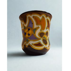 Op de afbeelding: Een bruine keramische vaas met een uitlopende bovenkant en een afgeronde basis. De vaas is versierd met een bloemmotief in tinten oranje, geel, paars en wit. De rand en de basis zijn donkerder bruin.