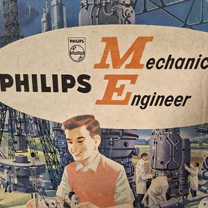 Op de afbeelding: Een Philips Mechanical Engineer constructieset doosdeksel met een centrale ovale afbeelding met de tekst Philips Mechanical Engineer. De illustratie toont een jong persoon die een model in elkaar zet met industriële machines op de achtergrond.