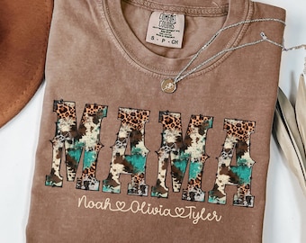 May include: A brown Comfort Colors t-shirt with the word "MAMA" in a bold, decorative font. The letters feature a mix of animal print and turquoise patterns. Below the word "MAMA" are the names "Noah", "Olivia", and "Tyler". A silver necklace rests on the shirt.
