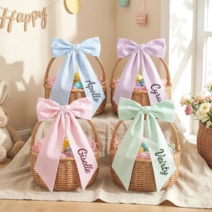 Puede incluir: Cuatro cestas de Pascua tejidas con lazos a rayas de colores pastel. Cada cesta tiene una etiqueta con nombre personalizado. Las cestas están llenas de huevos coloridos y papel decorativo. Decoraciones de Pascua en el fondo.
