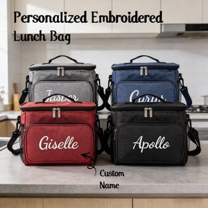 Peut inclure: Quatre sacs à lunch brodés personnalisés en gris, bleu marine, rouge et noir. Chaque sac a un nom brodé en blanc et une poche avant. Les sacs ont une poignée supérieure et une bandoulière amovible. Le texte en haut dit "Sac à lunch brodé personnalisé."