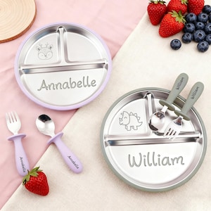 May include: Stainless steel divided plates with matching utensils. One plate is lavender with "Annabelle" engraved, the other is gray with "William". Each plate has a cartoon animal design. Utensils are lavender and gray.
