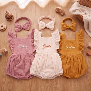 May include: Three sleeveless rompers with ruffled shoulders and matching bow headbands. The rompers are mauve, light pink, and mustard yellow, each featuring embroidered names: Emery, Gisella, and Sophia. The fabric has a textured, crinkled appearance.