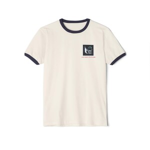 May include: A white t-shirt with a navy blue ringer neck and short sleeves. The shirt features a black and white graphic with the text "Journey Futures" in red.
