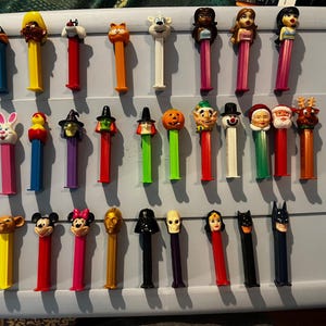 Puede incluir: Una colección de 30 figuras de juguete de plástico de colores, cada una con un diseño único. Las figuras están dispuestas en filas sobre una superficie blanca. Las figuras miden aproximadamente 7,5 cm de alto y están hechas de plástico. Las figuras son de diferentes colores y tienen una variedad de diseños, incluyendo animales, personajes de dibujos animados y figuras navideñas.