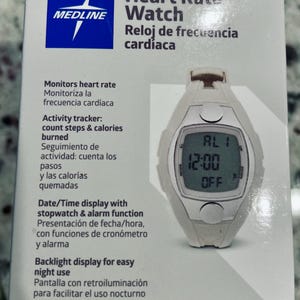 Pu&ograve; includere: Un orologio bianco Medline per la frequenza cardiaca con un display digitale che mostra l'ora 12:00 e la parola "OFF". L'orologio ha un quadrante rettangolare e si trova su una scatola bianca con testo in inglese e spagnolo.
