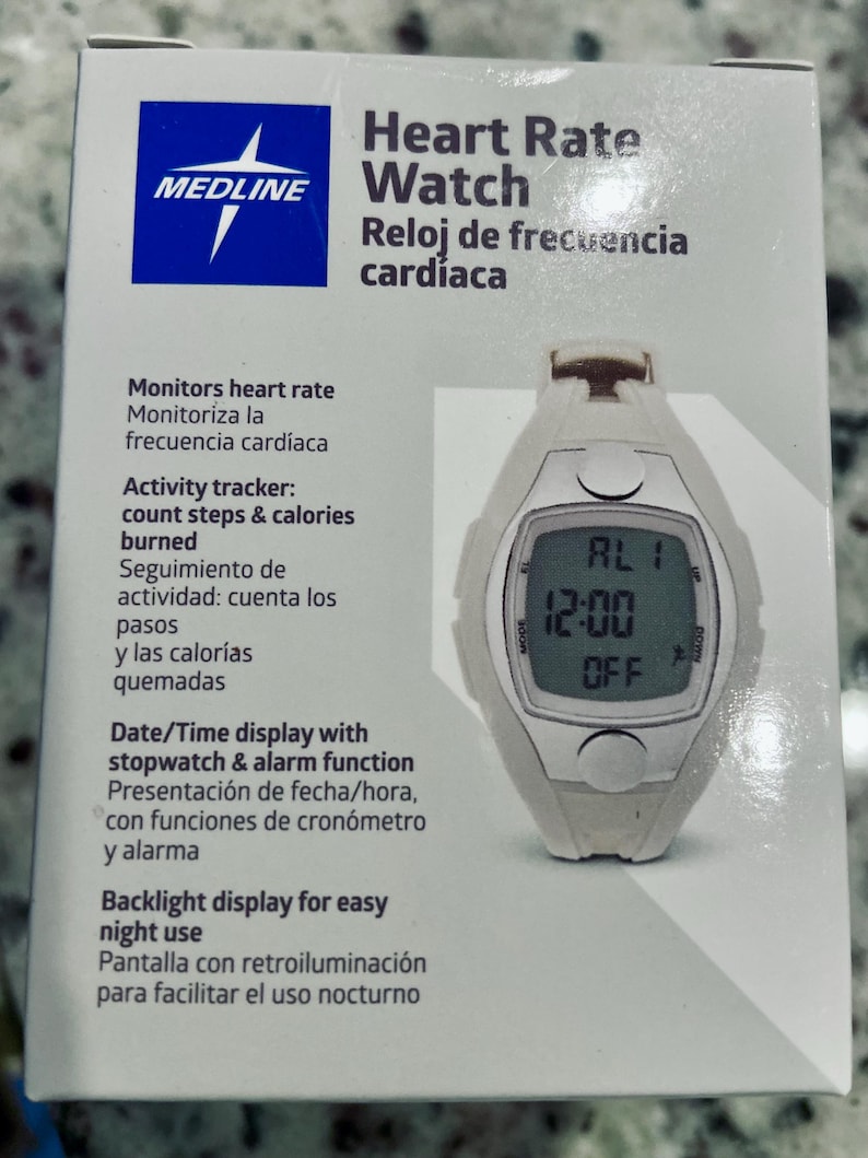Pu&ograve; includere: Un orologio bianco Medline per la frequenza cardiaca con un display digitale che mostra l'ora 12:00 e la parola "OFF". L'orologio ha un quadrante rettangolare e si trova su una scatola bianca con testo in inglese e spagnolo.