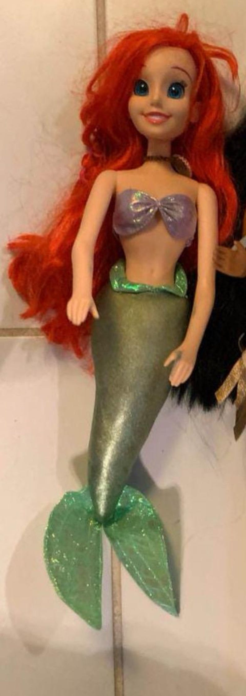 Pode incluir: Boneca de sereia com cabelo vermelho brilhante, olhos azuis e um sorriso. Ela usa um top roxo e uma cauda verde. Esta boneca &eacute; um brinquedo popular.