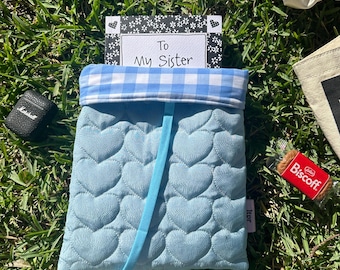 Può includere: Una pochette trapuntata blu con una fodera in tessuto a quadri blu e bianco. La pochette ha un nastro blu e un biglietto all'interno che dice "To My Sister".