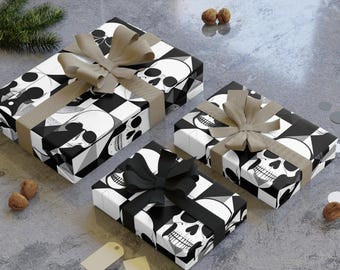 May include: Three gift boxes wrapped in black and white skull patterned paper with matching bows. The boxes are tied with tan and black ribbons. The gifts are arranged on a grey surface with decorative elements.