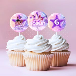 Könnte beinhalten: Drei Cupcakes mit weißem Zuckerguss und dekorativen Toppern. Die Topper zeigen ein Sterndesign mit der Zahl 6, Bilder von Personen und die Worte "Happy Birthday" und "Scarlet is turning 6". Die Cupcakes stehen auf einem hellrosa Hintergrund.