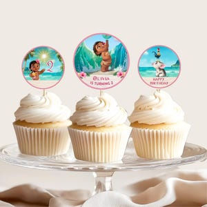Cupcakes displayed on a stand with circular toppers featuring Baby Moana, ocean waves, and birthday text in pink and tropical colors.