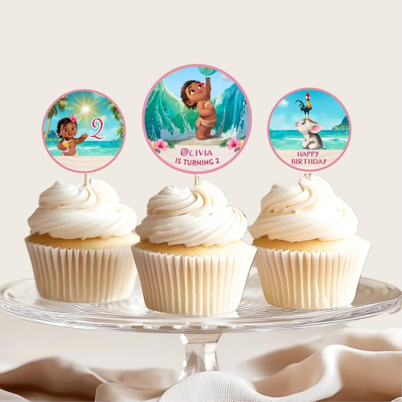 Cupcakes displayed on a stand with circular toppers featuring Baby Moana, ocean waves, and birthday text in pink and tropical colors.