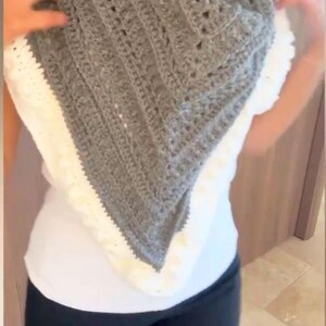 Peut inclure: Un châle en crochet gris et blanc de forme triangulaire. Le châle présente un motif texturé et une bordure blanche. Le texte "merveilles et créations" est visible en bas de l'image.