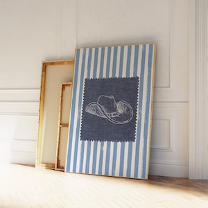 May include: A rectangular wall art print featuring a white and light blue vertical striped background. Centered on the print is a dark blue square patch with a jagged edge, displaying a white line drawing of a cowboy hat in the middle.