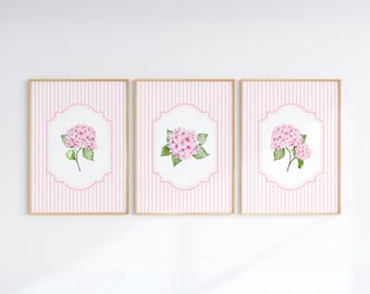 May include: A set of three rectangular wall art prints featuring light pink vertical stripes and a central white scalloped frame. Each print displays a watercolor illustration of a pink hydrangea flower with green leaves on a white background.
