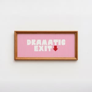 May include: A rectangular wooden frame containing a print with a light pink and white vertical striped background. The text "DRAMATIC EXIT" is printed in bold white capital letters, accompanied by a solid red downward-pointing arrow.