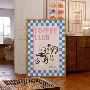 Puede incluir: Una lámina decorativa rectangular en un marco de madera con un borde de cuadros azules y blancos. El centro muestra el texto rosa COFFEE CLUB sobre un dibujo lineal negro de una taza de café y una cafetera, con el texto azul OPEN 24/7 debajo.