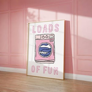 Puede incluir: Un póster blanco con una ilustración de lavadora rosa y el texto "LOADS OF FUN" en rosa.