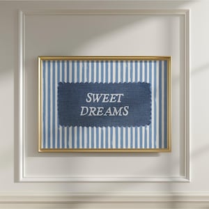 May include: A framed print with a gold border, featuring a blue and white striped background. A dark blue, scalloped-edged patch in the center displays the words "SWEET DREAMS" in white, creating a calming, decorative piece.