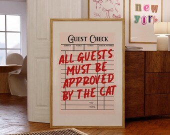Könnte beinhalten: Ein gerahmter Kunstdruck mit einem hellrosa Gästescheck-Design mit schwarzen Linien und Kopfzeilen. Der Text in fetter roter Schrift lautet: GUEST CHECK ALL GUESTS MUST BE APPROVED BY THE CAT. Der Druck befindet sich in einem hellen Holzrahmen.