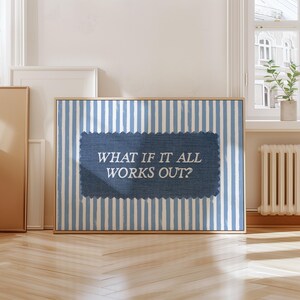 May include: A framed artwork with a blue and white striped background and a denim-textured center. The text "WHAT IF IT ALL WORKS OUT?" is displayed in white. The artwork is in a room with a window and wooden floor.