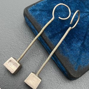 May include: A pair of silver earrings with a square-shaped pendant and a coiled wire design.