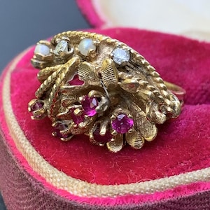 Peut inclure: Une bague en or avec un groupe de pierres précieuses roses et blanches. La bague est sertie d'un motif floral et a une bande texturée.