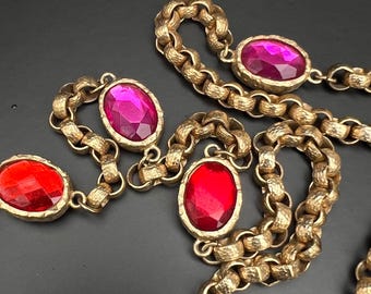 May include: A gold chain necklace with large oval-shaped red and pink glass stones. The chain is textured and has a chunky link design.