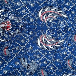 May include: A blue fabric featuring a dense batik pattern with white and red accents. The design includes stylized bird-like motifs, intricate floral shapes, and small white dots scattered across the surface, creating a complex, repeating visual texture.