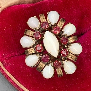 May include: A gold ring with a large white opal surrounded by smaller white opals and red gemstones.