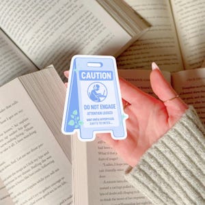 Op de afbeelding: Een lichtblauwe sticker in de vorm van een waarschuwingsbord, met de tekst "CAUTION" en "DO NOT ENGAGE". De sticker heeft een afbeelding van een persoon met een koptelefoon op een laptop. De tekst "ATTENTION LOCKED" en "WAIT UNTIL HYPERFOCUS SHIFTS TO ENTER..." zijn ook opgenomen.