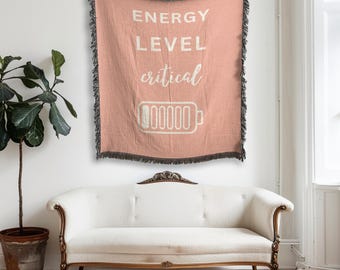 Pode incluir: Uma tapeçaria de parede tecida rosa com o texto "ENERGY LEVEL critical" e um ícone de bateria com uma barra de carga vazia.