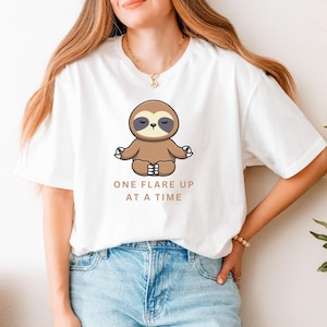 May include: White t-shirt with a cartoon sloth meditating and the text "One flare up at a time".