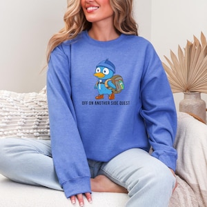 May include: A blue sweatshirt with a cartoon bird wearing a backpack and the text "Off on another side quest".