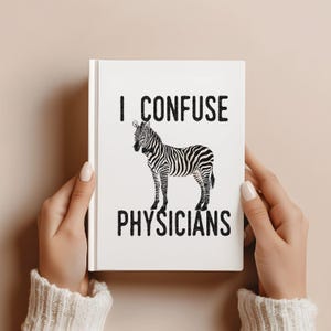 May include: White notebook featuring the text "I CONFUSE PHYSICIANS" above a black and white zebra illustration. The notebook is held by two hands with manicured nails.