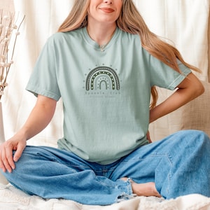 May include: A light blue t-shirt with a green, brown, and white rainbow design. The text "Sparkle Club" is written below the rainbow with the words "little in numbers" underneath.