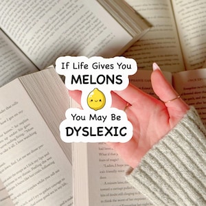 Pode incluir: Um autocolante branco com o texto "If Life Gives You MELONS You May Be DYSLEXIC" e uma ilustração de limão amarelo. O autocolante é segurado sobre livros abertos com texto.