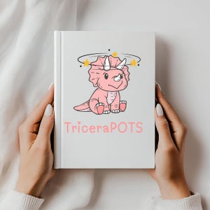 May include: A white book held by two hands, featuring a pink cartoon triceratops with a halo of stars. The text "TriceraPOTS" is printed in pink below the dinosaur illustration. The book has a clean, minimalist design.