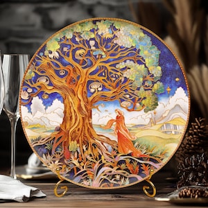 Puede incluir: Plato redondo decorativo con una ilustración detallada de un árbol y una mujer con un vestido naranja. El plato tiene un borde dorado y se exhibe sobre un soporte dorado. El fondo incluye un cielo azul y un paisaje.