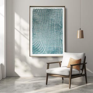 May include: Large framed artwork with a teal grid pattern on a white background. The artwork is displayed on a gray wall above a modern armchair with a white cushion and a small orange pillow. A gold pendant light hangs nearby.