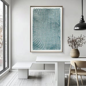 May include: A framed abstract art print featuring a teal-colored, woven-like pattern. The artwork is displayed in a room with white furniture, a wooden floor, and a large window. The print is rectangular and has a thin, brown frame.