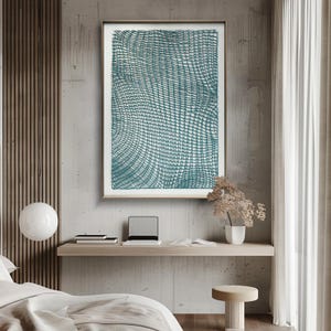 May include: A framed abstract art print featuring a teal and white grid pattern. The artwork is displayed on a concrete wall above a wooden desk with a laptop, books, and a small vase of dried flowers. The room has a modern, minimalist aesthetic.