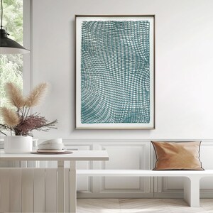 May include: A framed abstract art print featuring a teal and white woven pattern. The artwork is displayed in a room with a white table, bench, and a decorative vase with dried flowers. The frame is a light brown color.