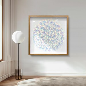 May include: A framed artwork featuring a circular design composed of numerous iridescent, triangular shapes. The artwork is encased in a light brown wooden frame and hangs on a white wall. A modern floor lamp with a large white globe and a cylindrical base stands nearby.